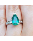 A Colombian emerald teardrop ring and princess cut band diamonds on a hand.