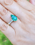 Hand wearing a white gold with a teardrop emerald ring against a blurred natural background.