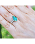 Hand wearing a white gold with a teardrop emerald ring against a blurred natural background.