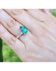 Pear-shaped emerald ring with princess cut diamonds on a 14K white gold band, worn on a hand.
