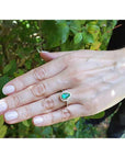 Hand wearing a teardrop emerald ring against a natural background.