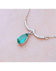 White gold necklace with a pear-shaped emerald and diamond-studded wavy bar.