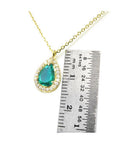 Pear-shaped natural emerald necklace with diamond halo in 14K yellow gold, shown next to a ruler.