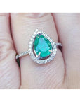 A natural colombian emerald teardrop ring with diamond halo on a finger.