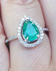 Emerald teardrop ring with diamond halo on a finger.
