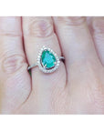 Teardrop emerald ring in 14K white gold with a diamond halo, worn on a finger.