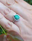 Hand wearing a white gold ring with a pear cut emerald against a natural background.
