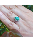 Teardrop emerald halo ring with diamonds on a hand, 14K white gold.
