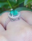 White gold ring with a natural emerald on a hand against a blurred green background.