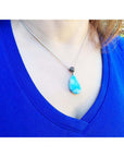 Larimar teardrop pendant on a sterling silver necklace, worn on a blue shirt.