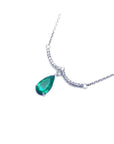 14K white gold necklace with a deep green pear-shaped emerald dangling from a diamond-studded wavy bar.