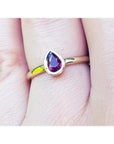 Woman's hand wearing a 14K yellow gold ring with a bezel-set teardrop natural ruby solitaire.