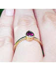 Gold ring with a teardrop natural ruby gemstone on a person's finger, underside view