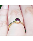 Woman's hand wearing a 14K yellow gold ring with a bezel-set teardrop natural ruby solitaire.