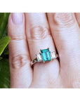 Emerald cut three stone ring with medium bluish green emerald and side baguette diamonds in 18k white gold.