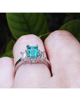 Emerald cut three stone emerald ring with baguette diamonds in 18K white gold on a finger.