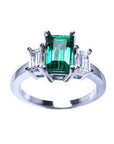 A women's emerald three stone ring in white gold, with a top profile view displaying side diamonds.