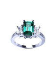 Emerald cut three stone ring with a medium bluish-green emerald and baguette diamonds in 18K white gold.