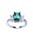 Emerald cut three stone ring with a medium bluish-green emerald and baguette diamonds in 18K white gold.