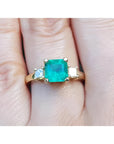 18K yellow gold three-stone ring with a square Colombian emerald and princess-cut side diamonds.