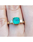 18K yellow gold three-stone ring with a square Colombian emerald and princess-cut side diamonds.