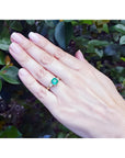 18K yellow gold three-stone ring with a square emerald and princess-cut side diamonds on a hand.