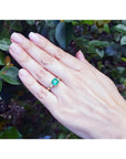 18K yellow gold three-stone ring with a square emerald and princess-cut side diamonds on a hand.