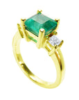 This 18k yellow gold three stone emerald ring is on a tilted position to show the top stone and side diamond profile.