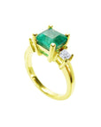 This 18k yellow gold three stone emerald ring is on a tilted position to show the top stone and side diamond profile.