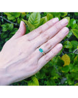 1.01 ct rectangular bluish-green emerald ring with natural diamond accents set in 14K yellow gold on a hand.