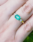 Emerald three stone ring on a hand with a blurred green background