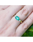 1.01 ct rectangular emerald ring with two diamond accents set in 14K yellow gold on a hand.