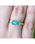 A 14k yellow gold emerald three stone ring with side diamonds on a person's finger.