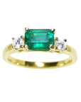 The topside of this three stone emerald ring displays the main stone with side natural diamonds.