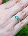 Hand wearing an emerald ring with a green leafy background
