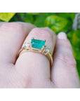1.01 ct rectangular emerald ring with diamond accents set in 14K yellow gold on a finger.