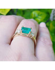 1.01 ct rectangular emerald ring with diamond accents set in 14K yellow gold on a finger.