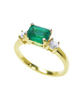 A partial lateral view of a rectangular colombian emerald with side diamonds in yellow gold.