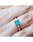 A natural colombian emerald square cut and side diamonds ring on a hand.