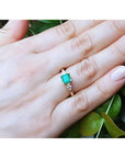 14K yellow gold three-stone emerald ring with pear-shaped side diamonds on a hand.