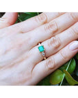 14K yellow gold three-stone emerald ring with pear-shaped side diamonds on a hand.