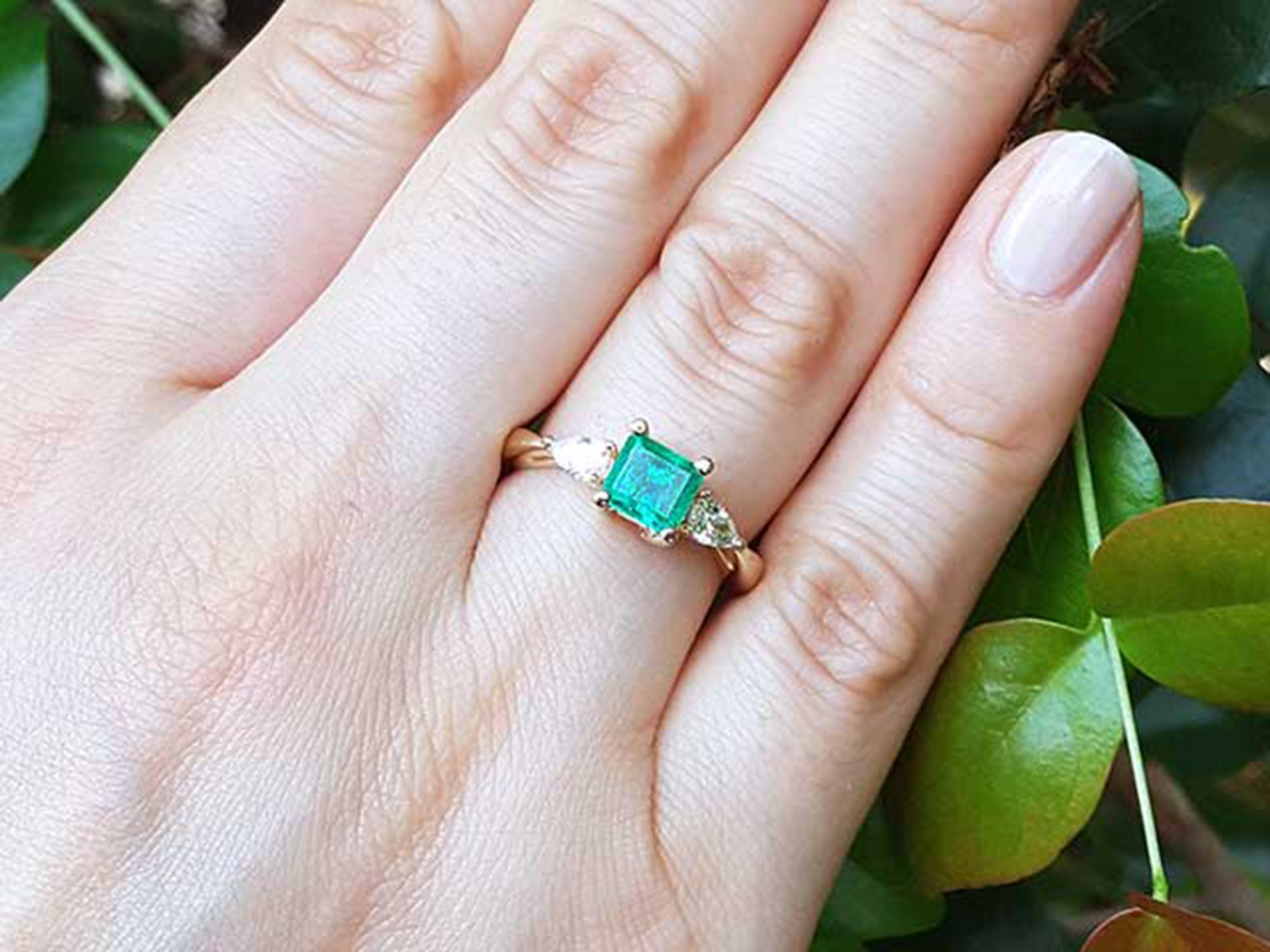 Gold ring with a natural emerald on a hand against a natural background.