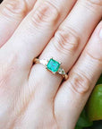 Gold ring with a natural emerald on a hand against a natural background.