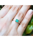 14K yellow gold three-stone emerald ring with pear-shaped side diamonds on a hand.