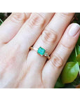 14K yellow gold three-stone emerald ring with pear-shaped side diamonds on a hand.