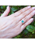 14k yellow gold three-stone ring with a round bluish-green emerald and two side diamonds on a hand.