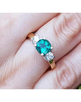 A women's round cut colombian emerald three stone ring with side natural diamonds on a finger.