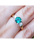 A women's emerald three stone ring side diamonds on a finger.