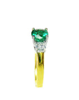 A side profile of this gold ring with a round emerald and smaller diamonds on a white background.