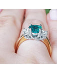 1.12 ct round cut bluish-green emerald three-stone ring with side diamonds in 14k white and yellow gold.